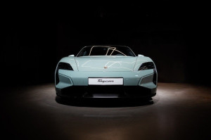 Front view of a white Porsche Taycan sports car displayed under dramatic lighting in a dark showroom.