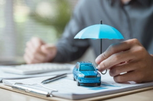 Hand holding a blue umbrella over a model SUV on insurance documents.
