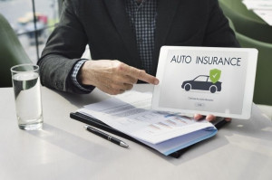 Business professional holding a tablet displaying an auto insurance webpage with a protected car icon during a client meeting