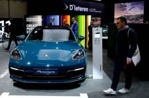 Blue Porsche luxury sports sedan showcased at an automotive exhibition with visitors viewing the vehicle.