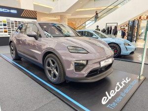 A lavender-colored Porsche Macan Electric displayed in a showroom alongside another Porsche vehicle.