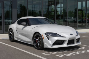 White 2026 Toyota Supra sports car with black alloy wheels parked in front of an auto dealership.